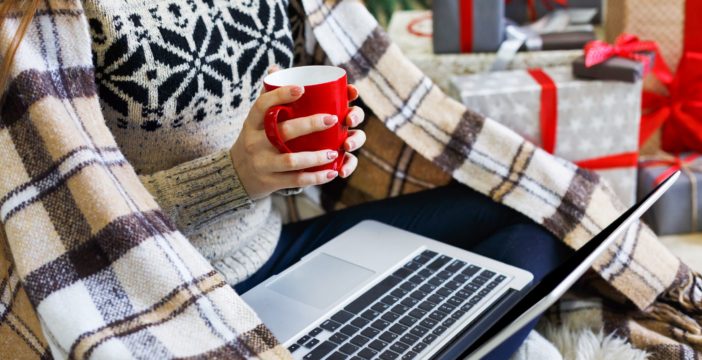 women with blanket and cup of coffee holiday shopping on her laptop