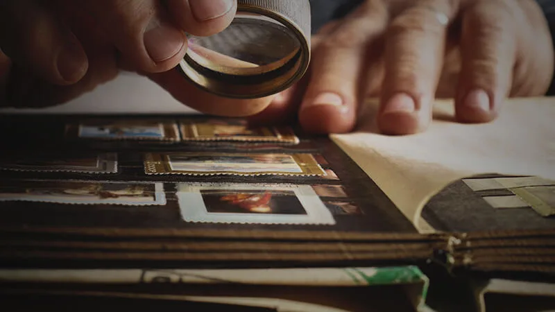 man holding magnifying glass to a stamp