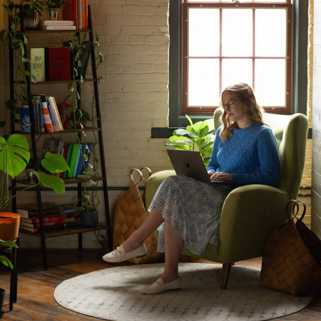 Tower Marketing employee completing client work in a accent chair in a plant-filled room.