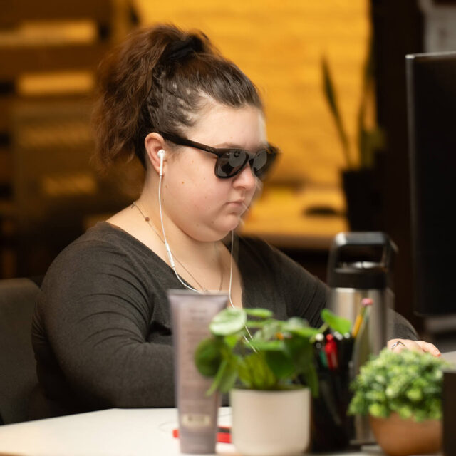 Tower Marketing employee wearing sunglasses and headphones working on a blog for a client at a desk in the Tower Marketing office