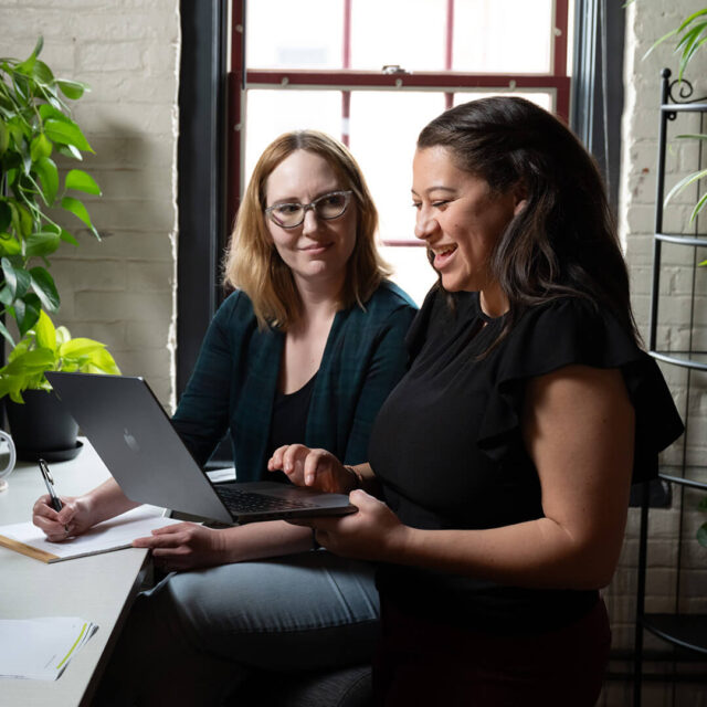 Two Tower Marketing employees discussing content creation for a client on a desk with plants in the Tower Marketing office