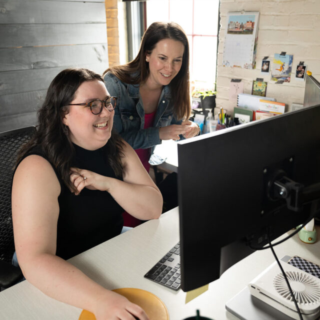 Two Tower Marketing employees discussing client marketing strategy around a desktop computer on a modern desk