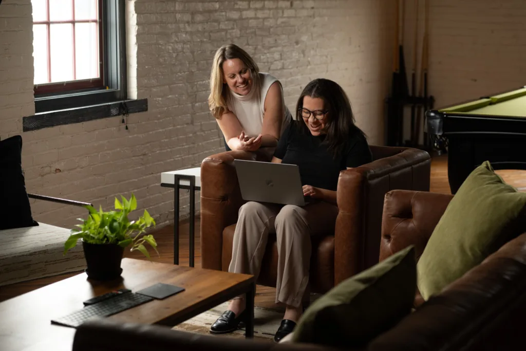 Two marketers discuss Pinterest vs Facebook ads around a laptop.