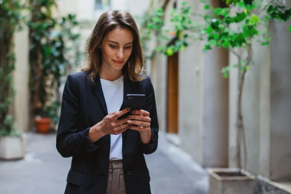 A woman checking her emails on a phone while standing outside.
