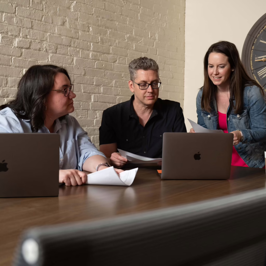 Three employees sit at a table at an engineering marketing agency