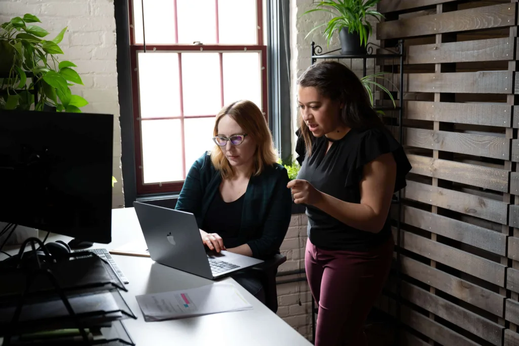 Two healthcare digital marketing agency employees look at a laptop at someone's desk