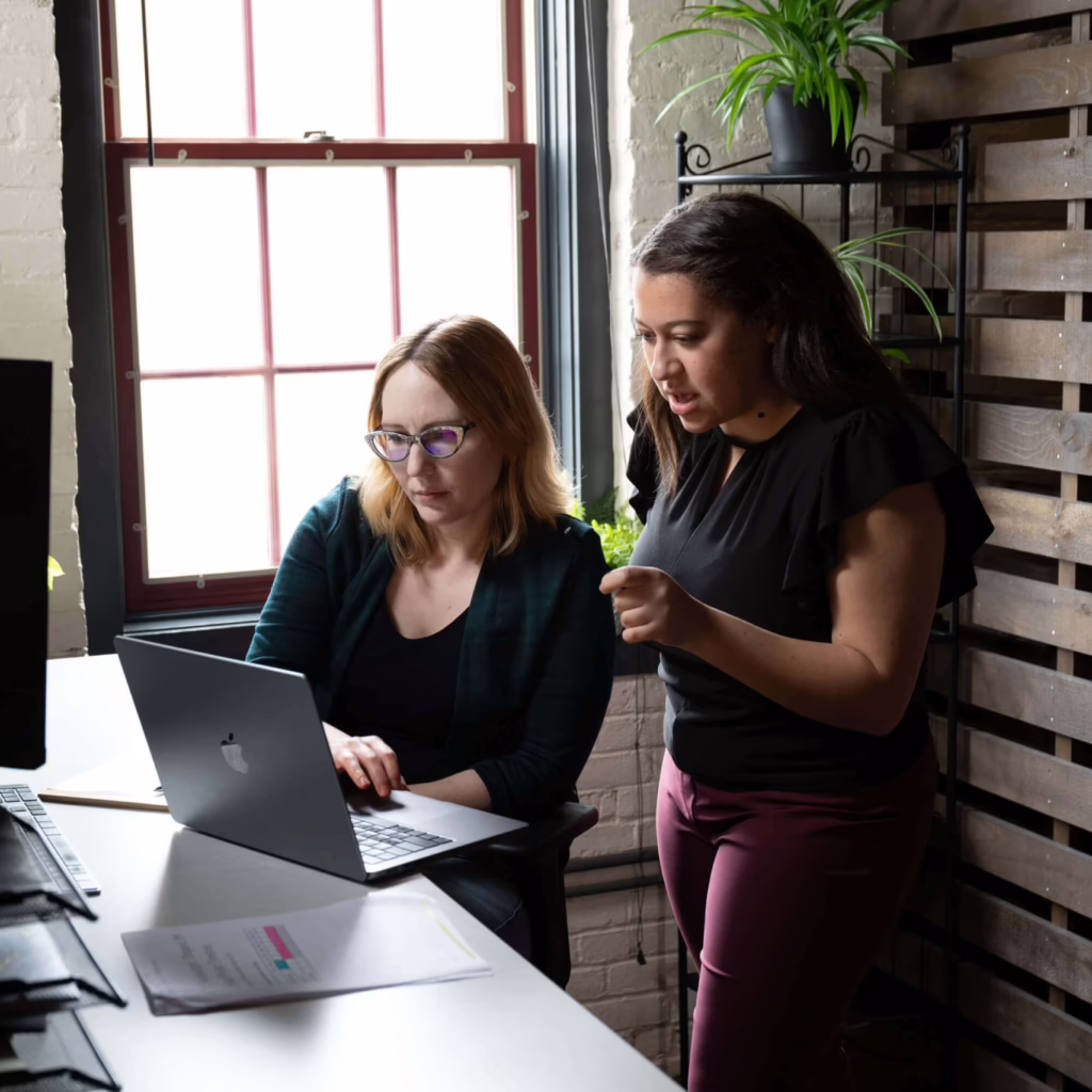 Two healthcare digital marketing agency employees look at a laptop at someone's desk