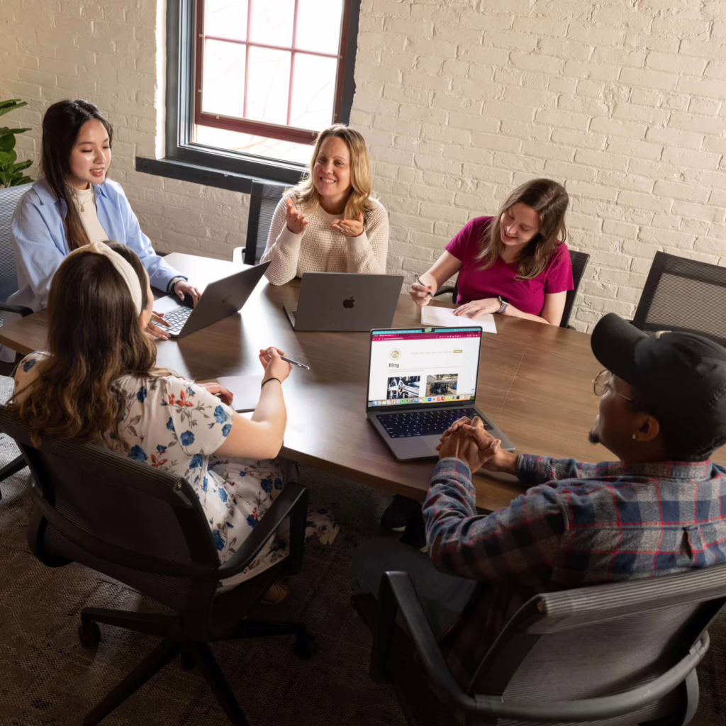 Five manufacturing digital marketing agency employees sit around a table