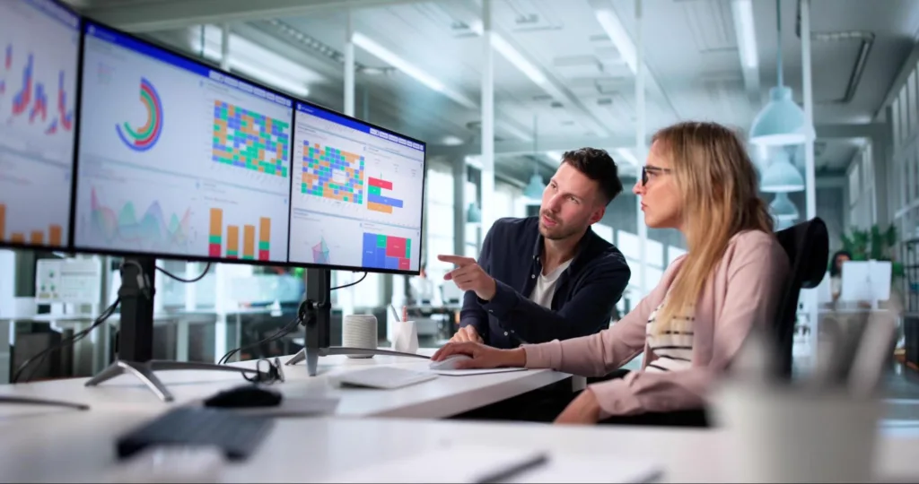 business professionals sitting at a desk and collaborating while reviewing a detailed content marketing analytics dashboard across a multi-monitor display.