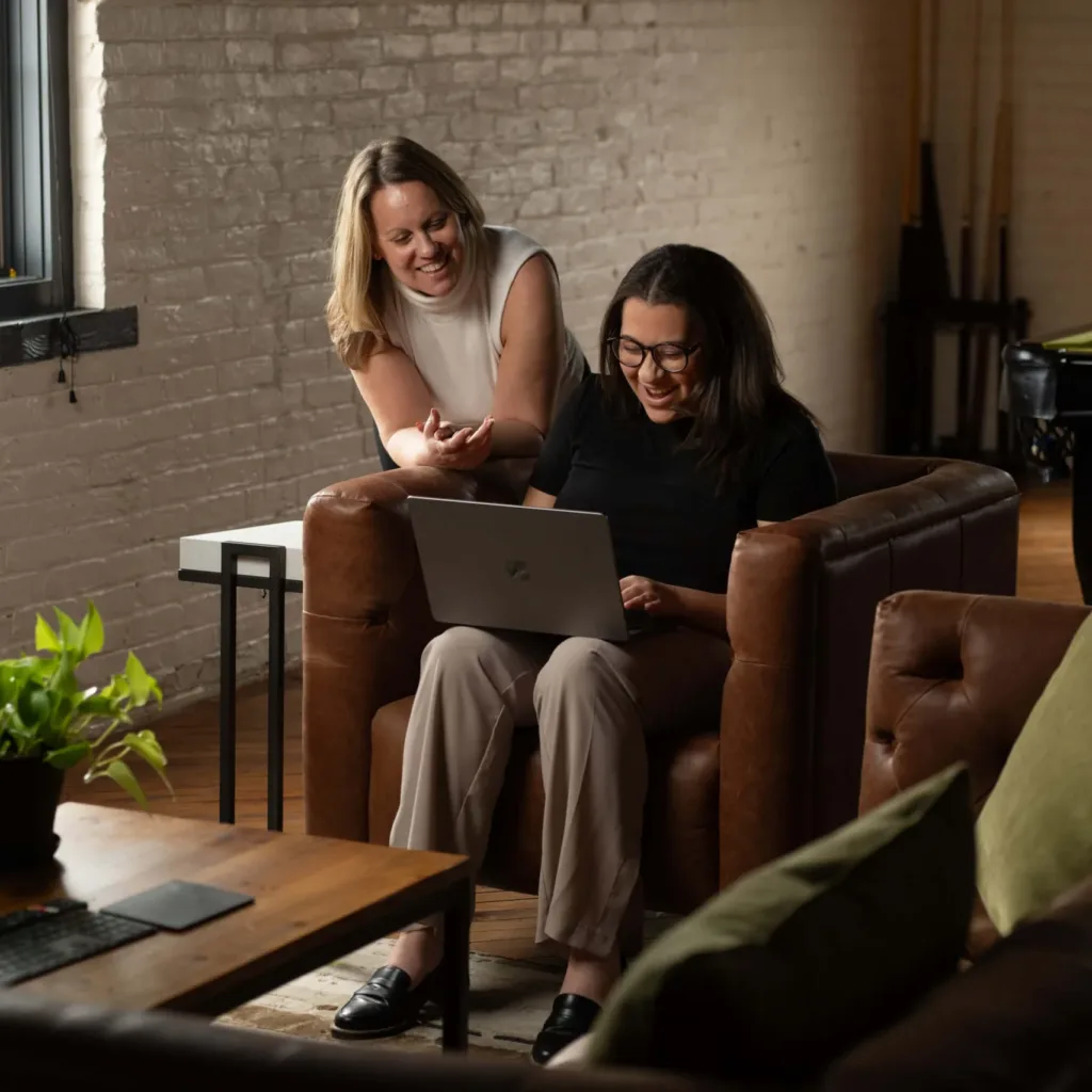 Two employees of a senior living digital marketing agency look at a laptop together